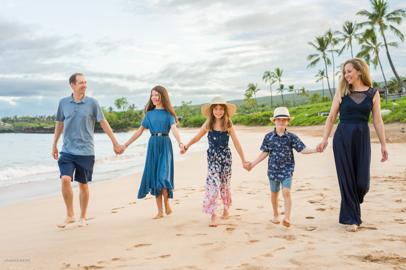 A family of five walking hand in hand along the shoreline during a morning session in Wailea