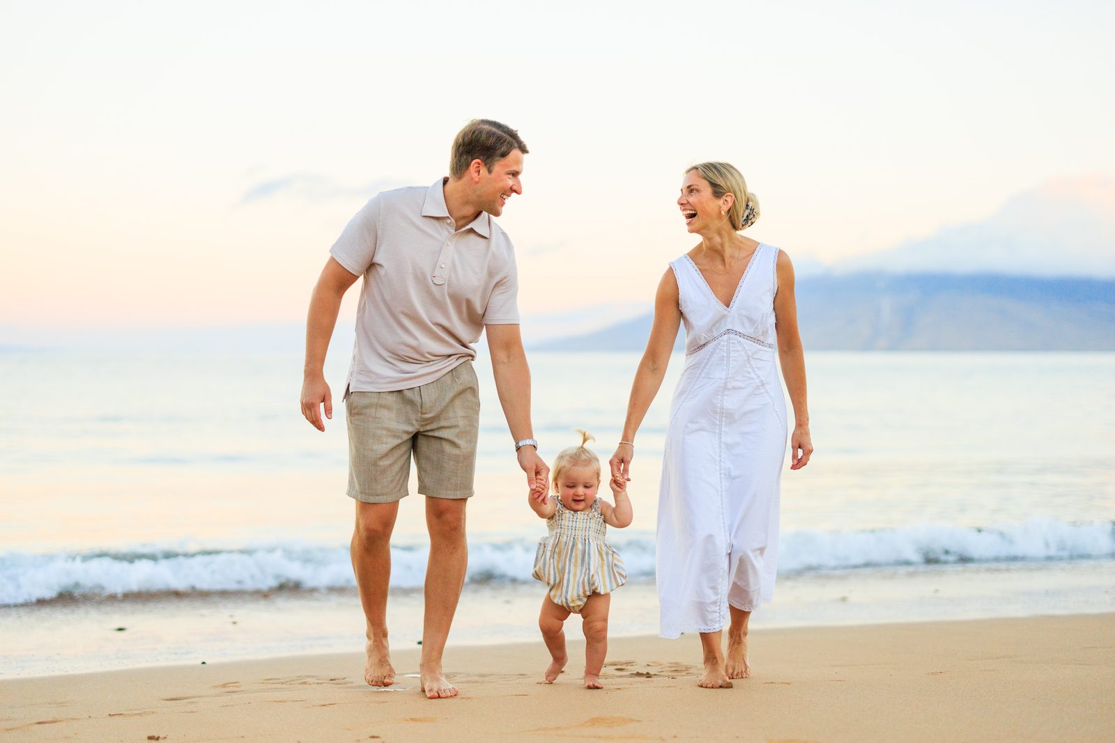 A young family walking hand in hand with their toddler along the shore at sunrise in Wailea