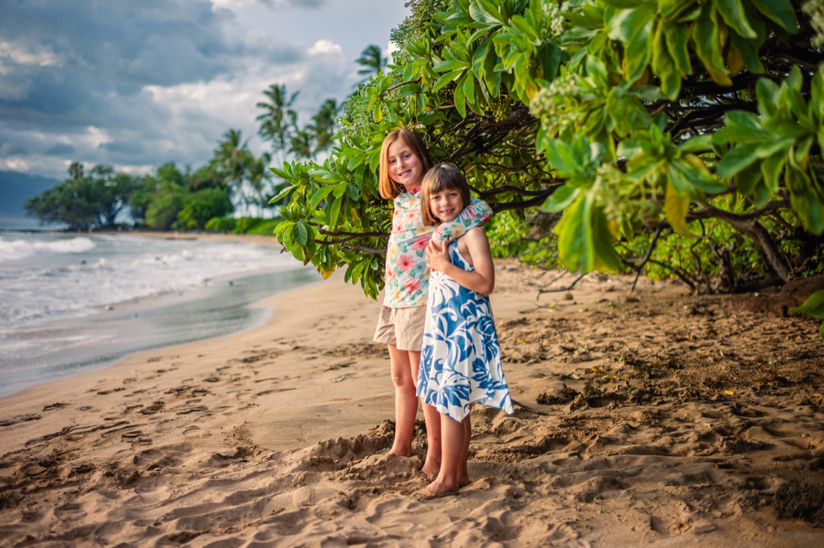Two children photographed beneath tropical greenery beside a Maui beach