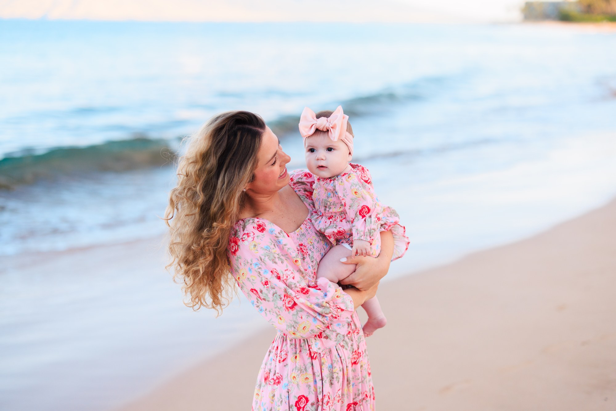 A mother holding her baby beside the ocean at sunrise