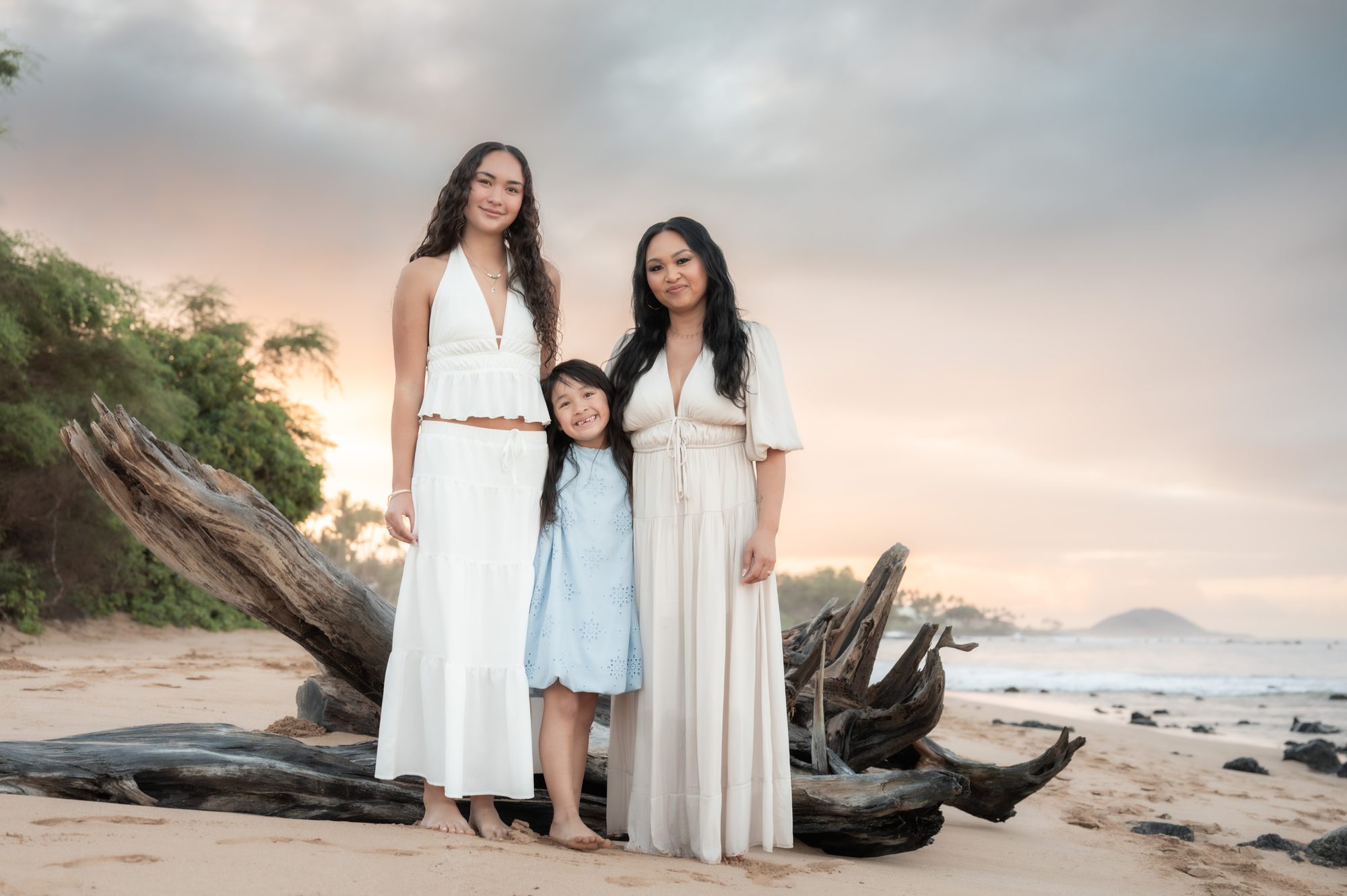 A mother and her two daughters beside driftwood at sunrise in Wailea