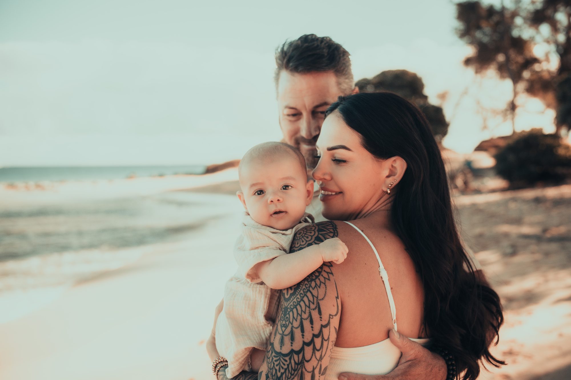 Parents holding their baby in warm sunrise light on a Maui beach