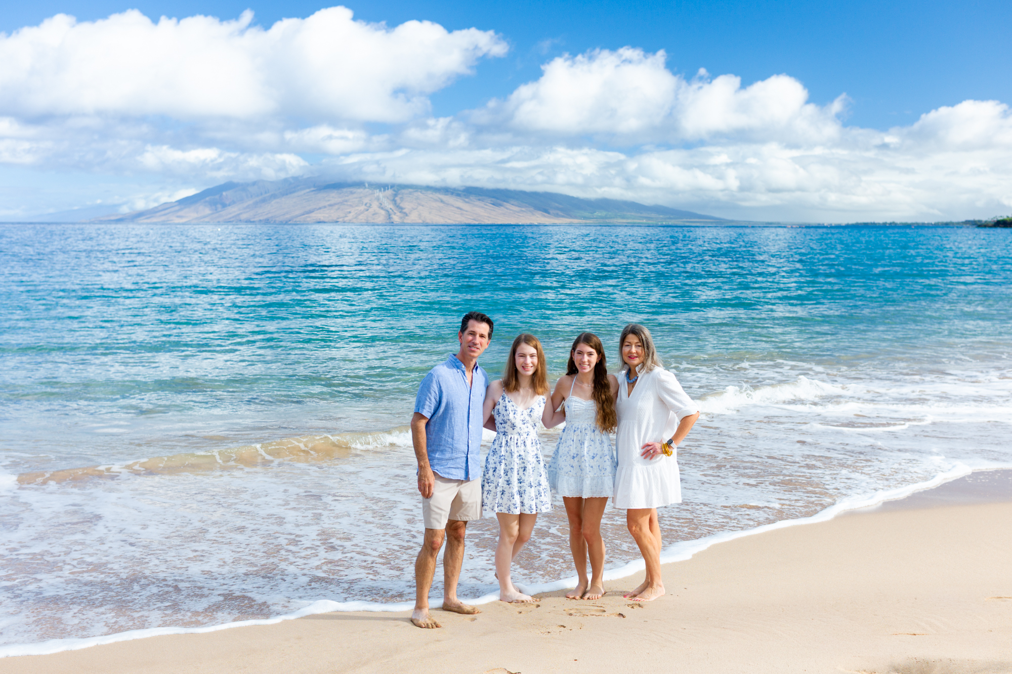 A family standing beside turquoise water with West Maui in the distance